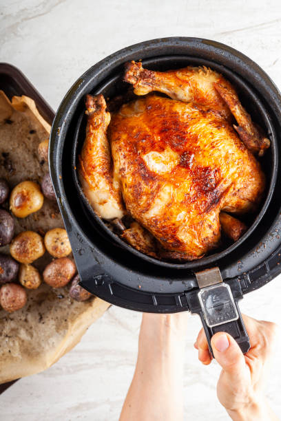 A perfectly roasted chicken in an air fryer being held by a hand, with roasted baby potatoes on the side.