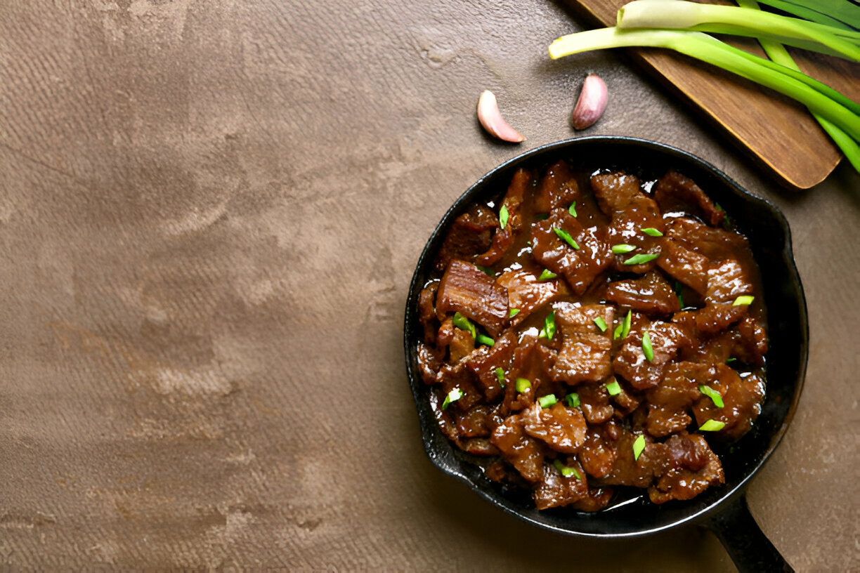 A cast iron skillet filled with flavorful sliced beef garnished with green onions on a textured surface.