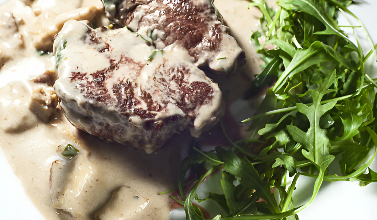 A plated dish featuring a serving of beef steak with creamy sauce alongside fresh arugula on a white plate.