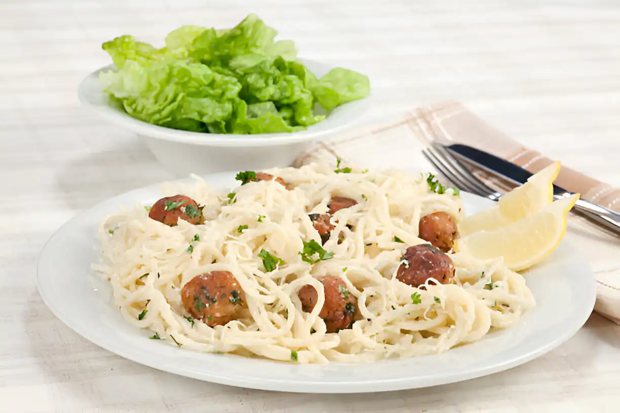 A plate of spaghetti with meatballs garnished with parsley and served with lemon wedges, alongside a bowl of fresh lettuce.