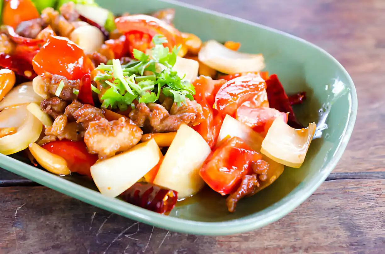 A colorful dish of stir-fried vegetables and meat topped with fresh herbs in a green bowl.