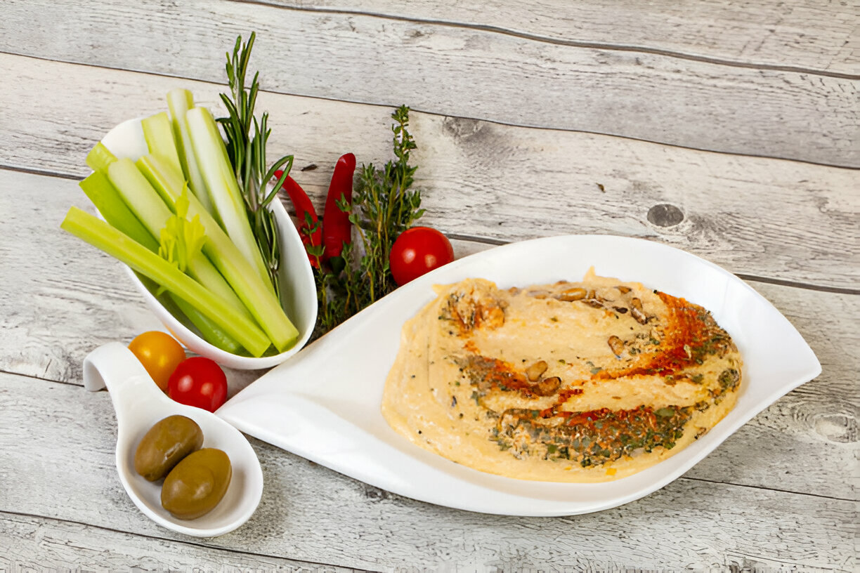A plate of hummus topped with herbs and spices, served with fresh celery and cherry tomatoes on the side.