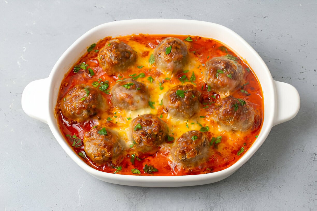 A dish of meatballs covered in sauce and melted cheese, garnished with parsley.