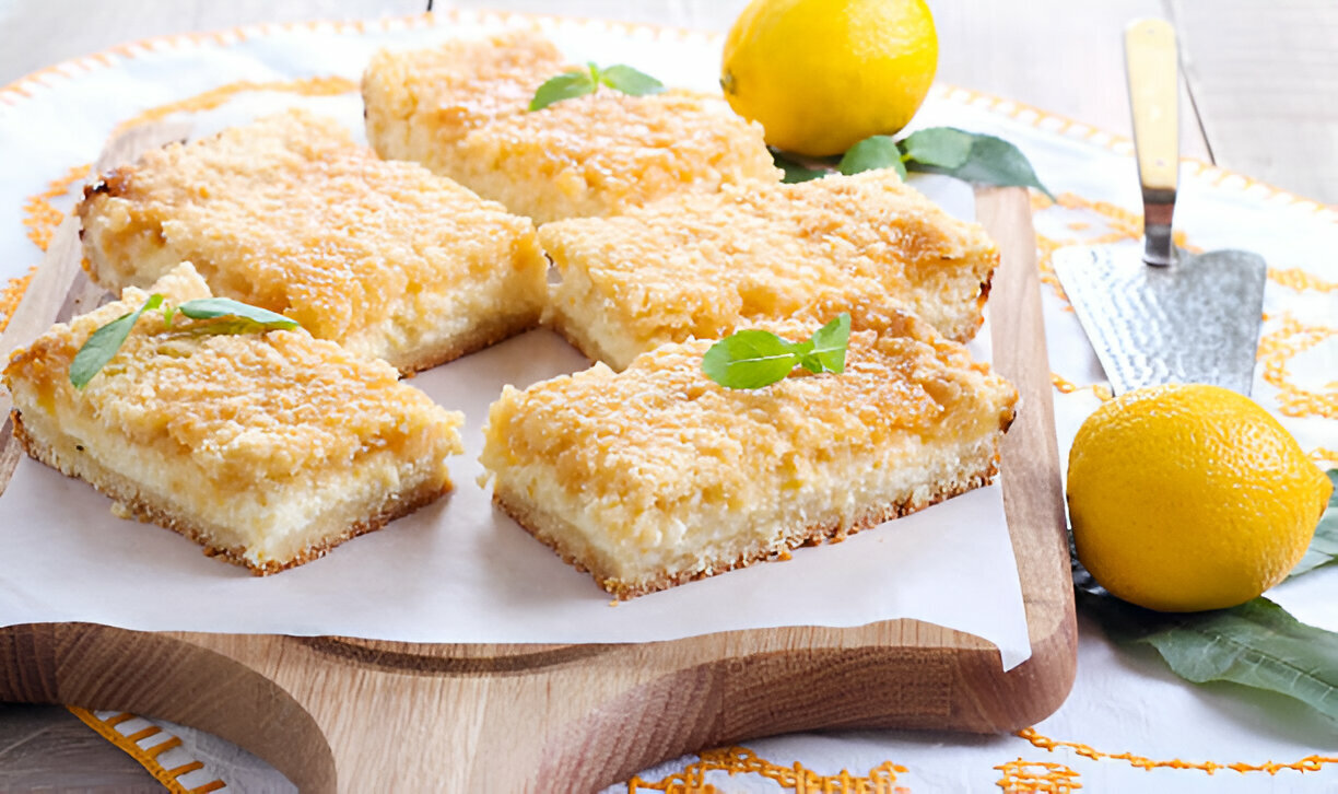 Lemon dessert bars arranged on a wooden serving board with fresh lemons and mint leaves.