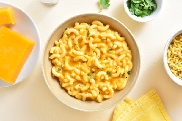 A bowl of creamy macaroni and cheese with a sprinkle of herbs, surrounded by cheese blocks and fresh cilantro.