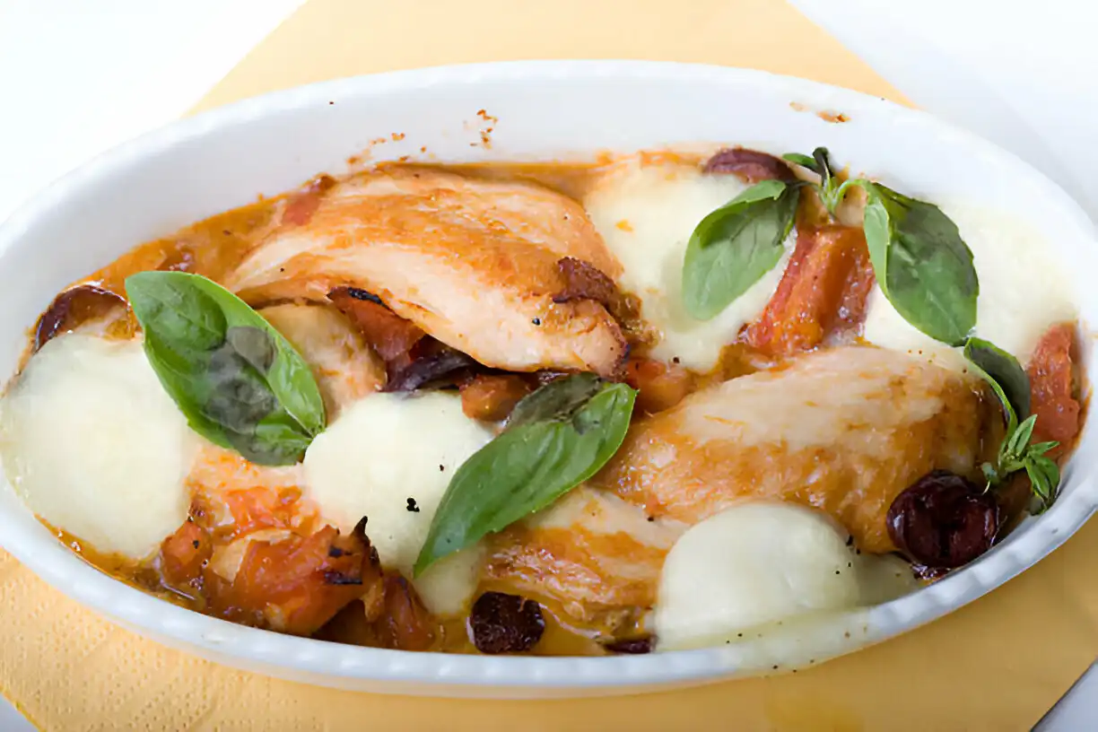 A delicious serving of baked chicken with cheese, tomatoes, and basil in a white dish