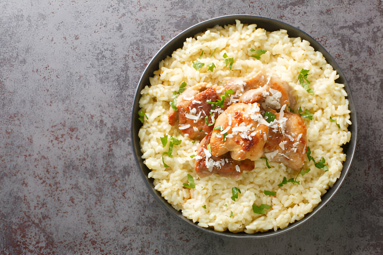 A bowl of creamy risotto topped with chicken and garnished with parsley and grated cheese.