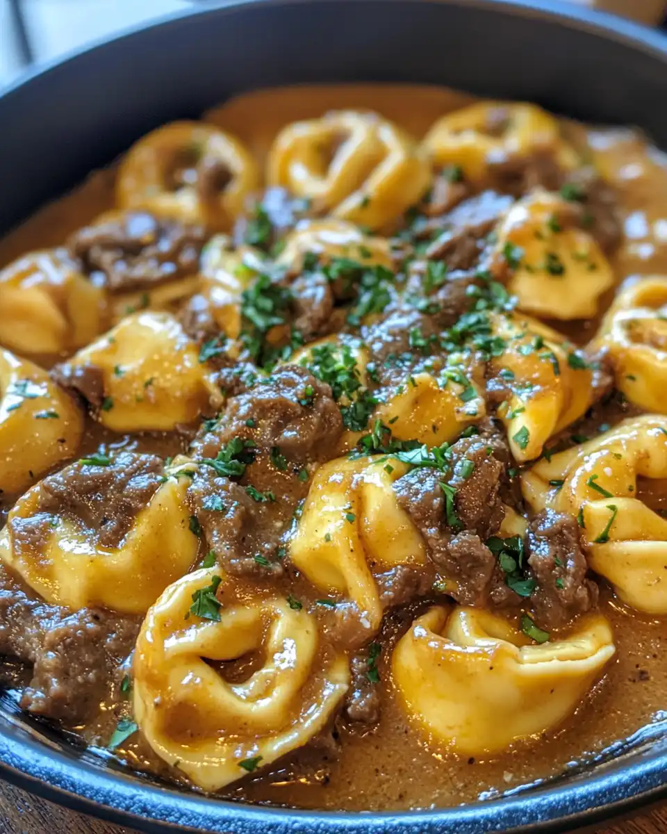Ingredients for cheesesteak tortellini including beef, provolone cheese, and garlic in skillet