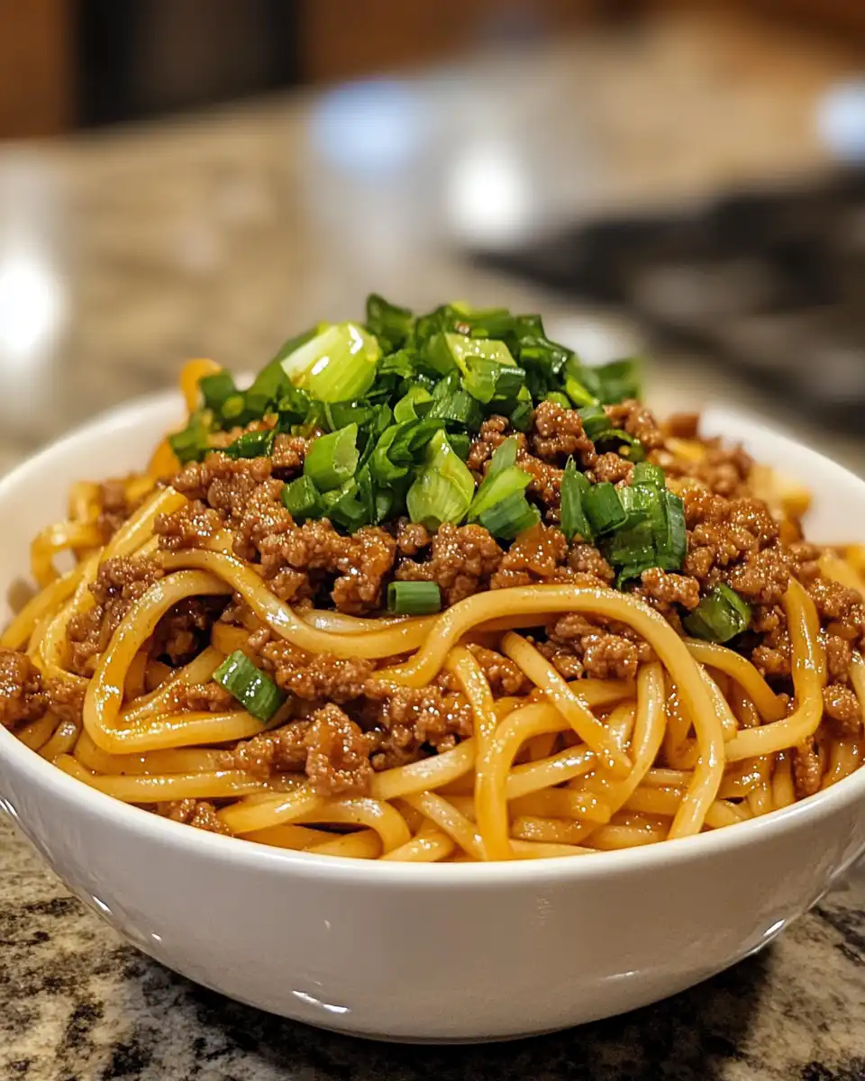 Serving bowl of finished Mongolian ground beef noodles garnished with green onions